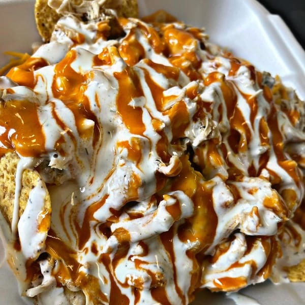 Chubbfathers' loaded nachos with white and orange sauces drizzled over tortilla chips and meat.