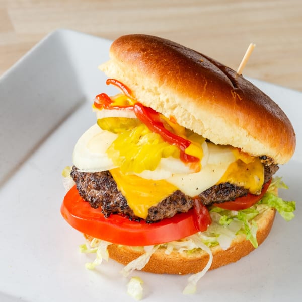 A Chubbfathers burger with melted cheese, fresh lettuce, tomato, onions, pickles, ketchup, and mustard.