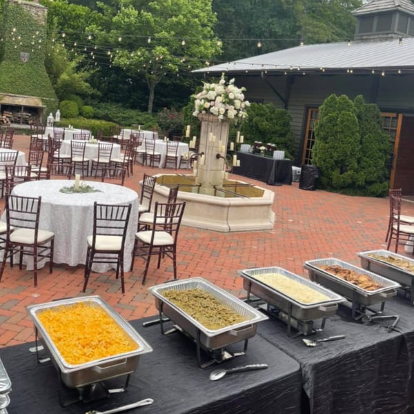 Outdoor patio with buffet tables, round dining tables, a fountain, and string lights overhead.