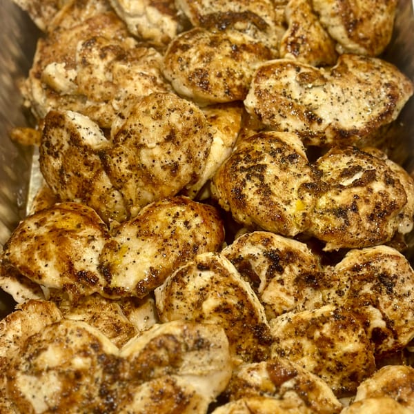 Close-up of many grilled chicken pieces, seasoned with pepper and spices, in a serving tray.