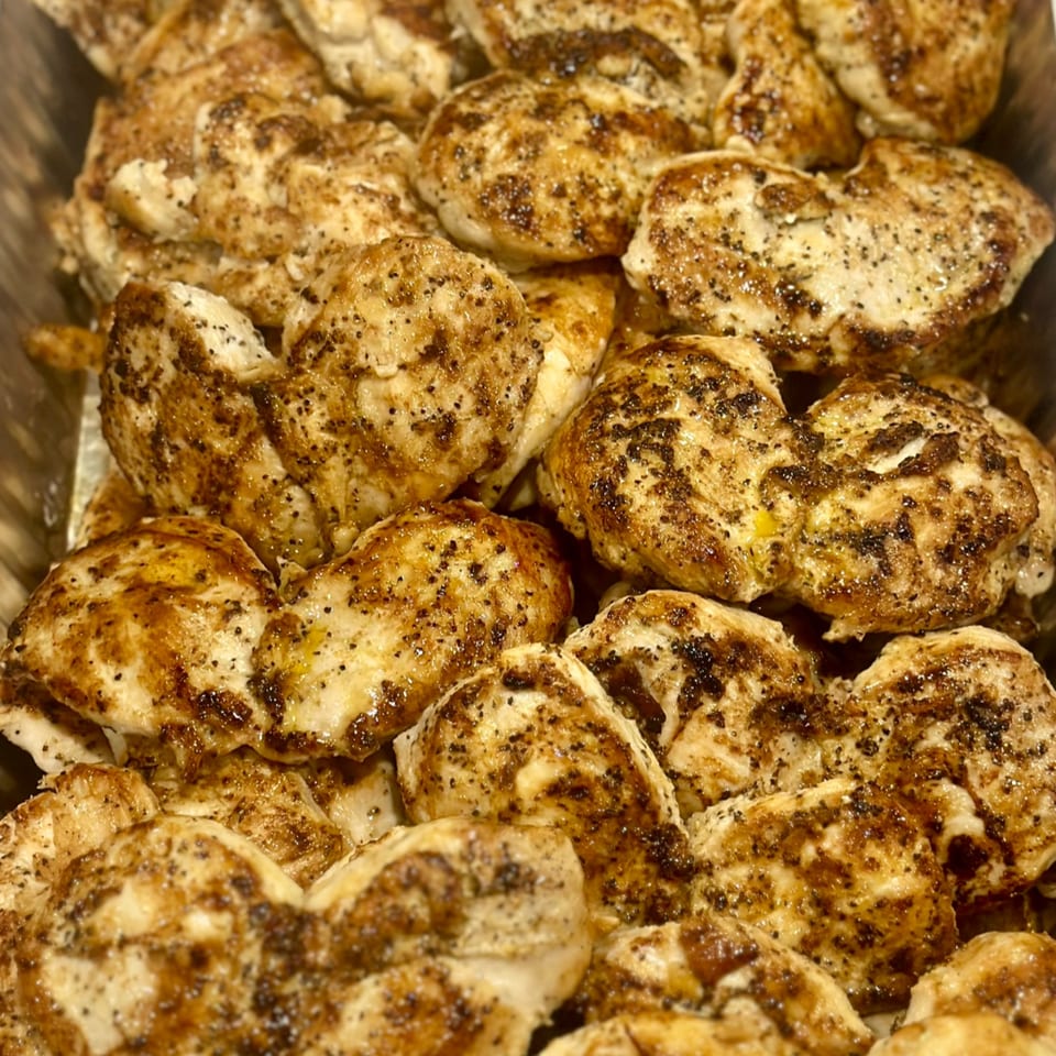 Close-up of many grilled chicken pieces, seasoned with pepper and spices, in a serving tray.