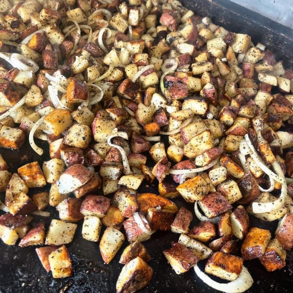 Close-up of seasoned, diced potatoes and sliced onions sizzling on a dark griddle.
