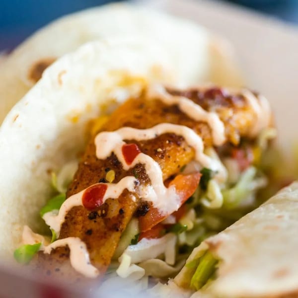 Close-up of a Chubbfathers fish taco with white sauce, red sauce, lettuce, and tomatoes.